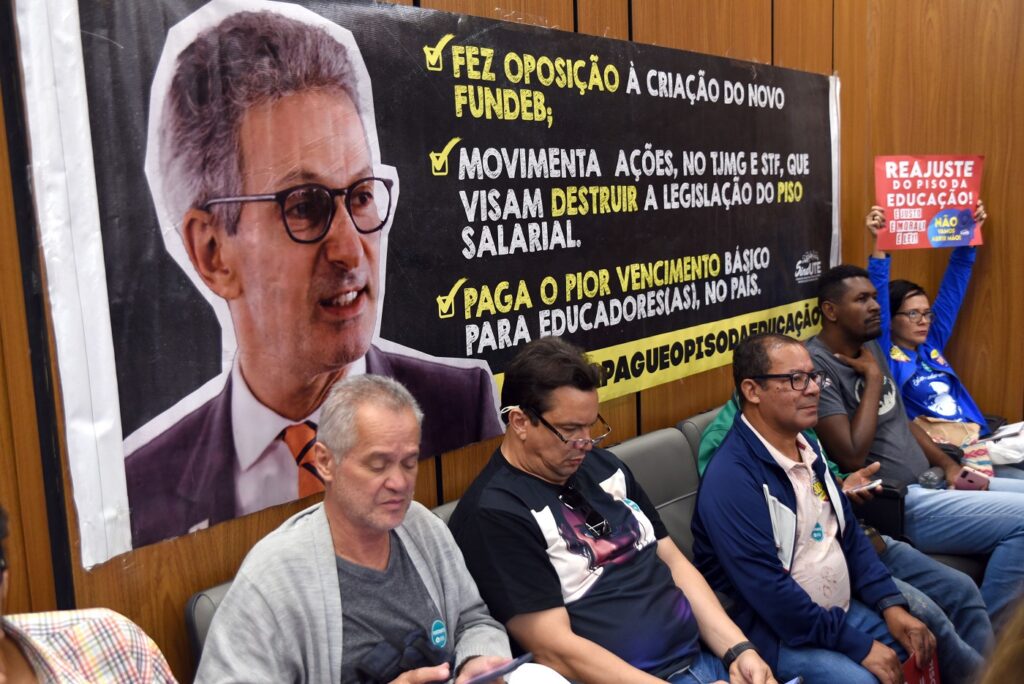 Cartaz trazido por profissionais de escolas públicas  que reivindicam o piso da educação pontua ações de Zema contra a melhora das instituições de ensino. 